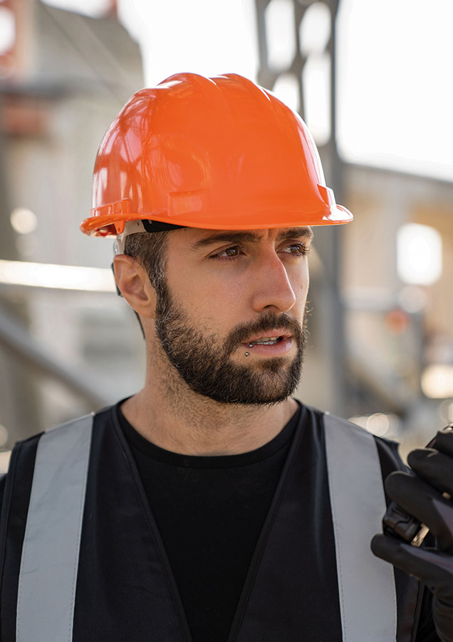 Erwachsener Bauarbeiter trägt einen orange-farbenen Korntex Schutzhelm auf einer Baustelle