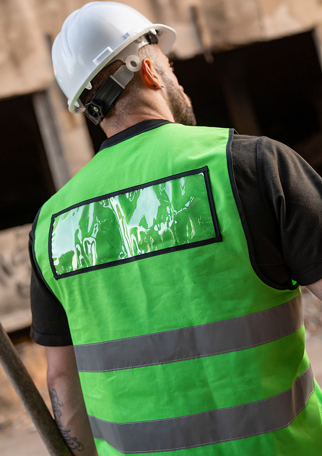 Ein Mann trägt eine grüne Korntex-Warnweste, und auf dem Rücken sieht man das schwarze Korntex-ID-Pocket mit transparentem Sichtfeld
