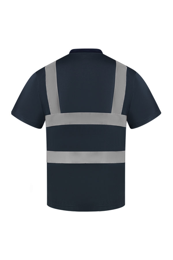 Erwachsene Frau steht in signal-orangenem Korntex Warnschutz-T-Shirt und weißem Schutzhelm vor einem Gerüst auf einer Industriebaustelle