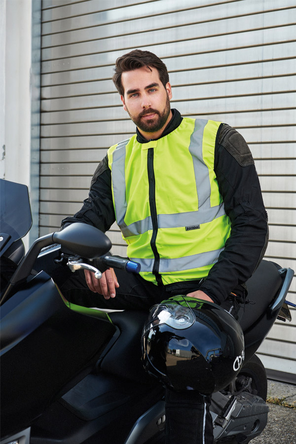 Erwachsener Motorradfahrer in signal-gelber Korntex Warnweste sitzt auf einem Motorrad vor einer Garage