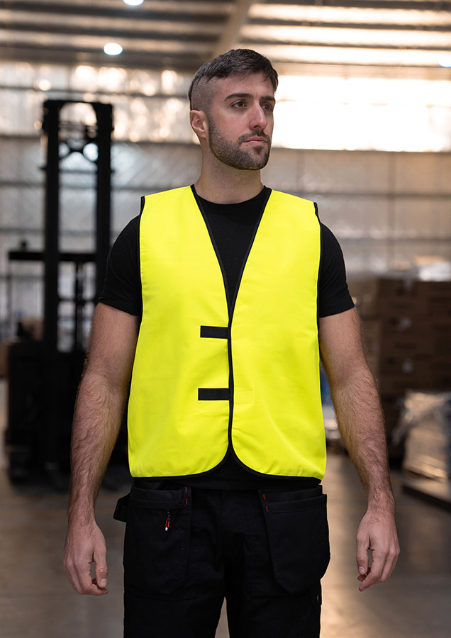 Erwachsener Arbeiter steht in signal-gelber Korntex Warnweste in einerm Lager