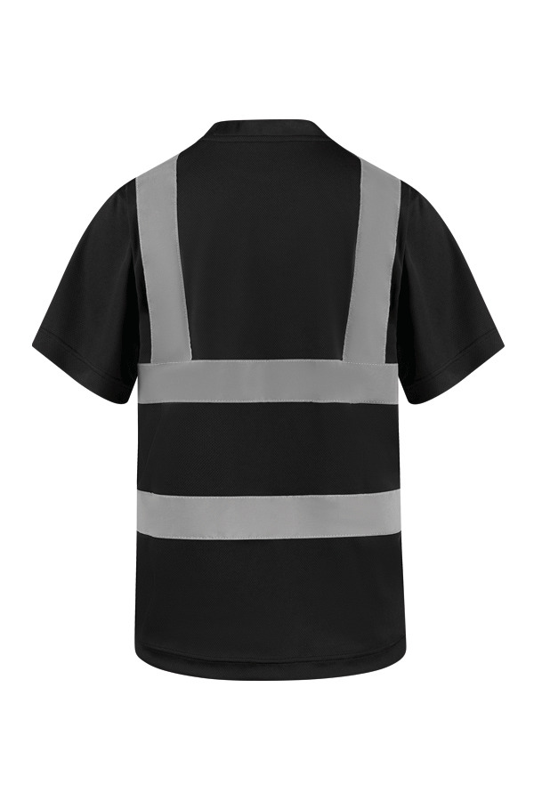 Erwachsene Frau steht in signal-orangenem Korntex Warnschutz-T-Shirt und weißem Schutzhelm vor einem Gerüst auf einer Industriebaustelle