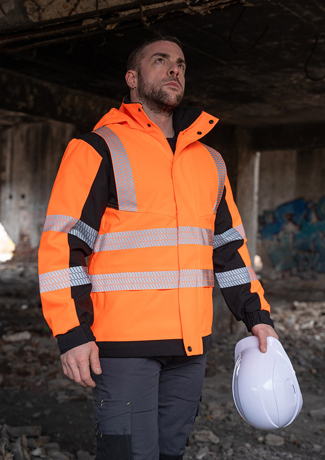 Erwachsener in orangefarbener Korntex-Softshell-Regenjacke mit Reflexstreifen auf einer Baustelle